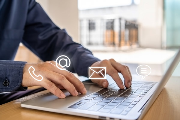 Eine Person tippt auf einer Laptop-Tastatur, umgeben von Symbolen für Telefon, E-Mail und Chat.